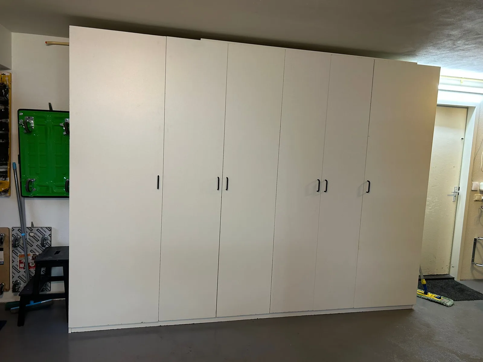 A real self-built garage storage cabinet in white melamine, floor to ceiling, with six doors and black bar handles